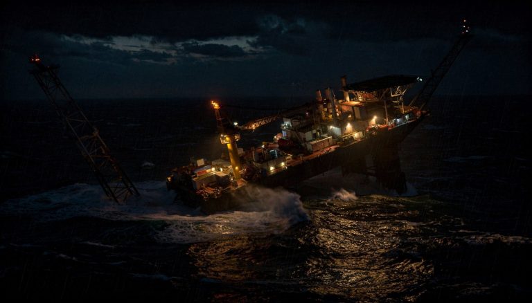 Offshore oil platform partially capsized at night in rough seas