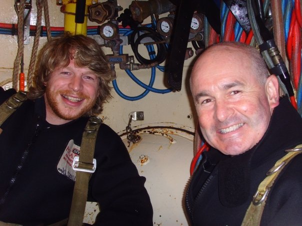 Two commercial divers smiling inside a saturation chamber, both over 35